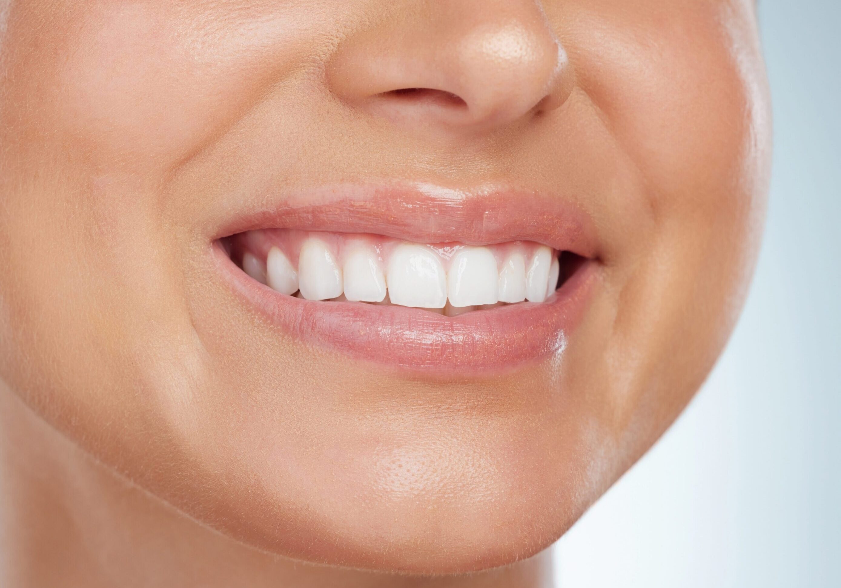 Closeup of unknown woman smiling with white teeth after a whitening treatment. Happy caucasian model isolated against grey background in a studio and showing perfect dental hygiene routine and care