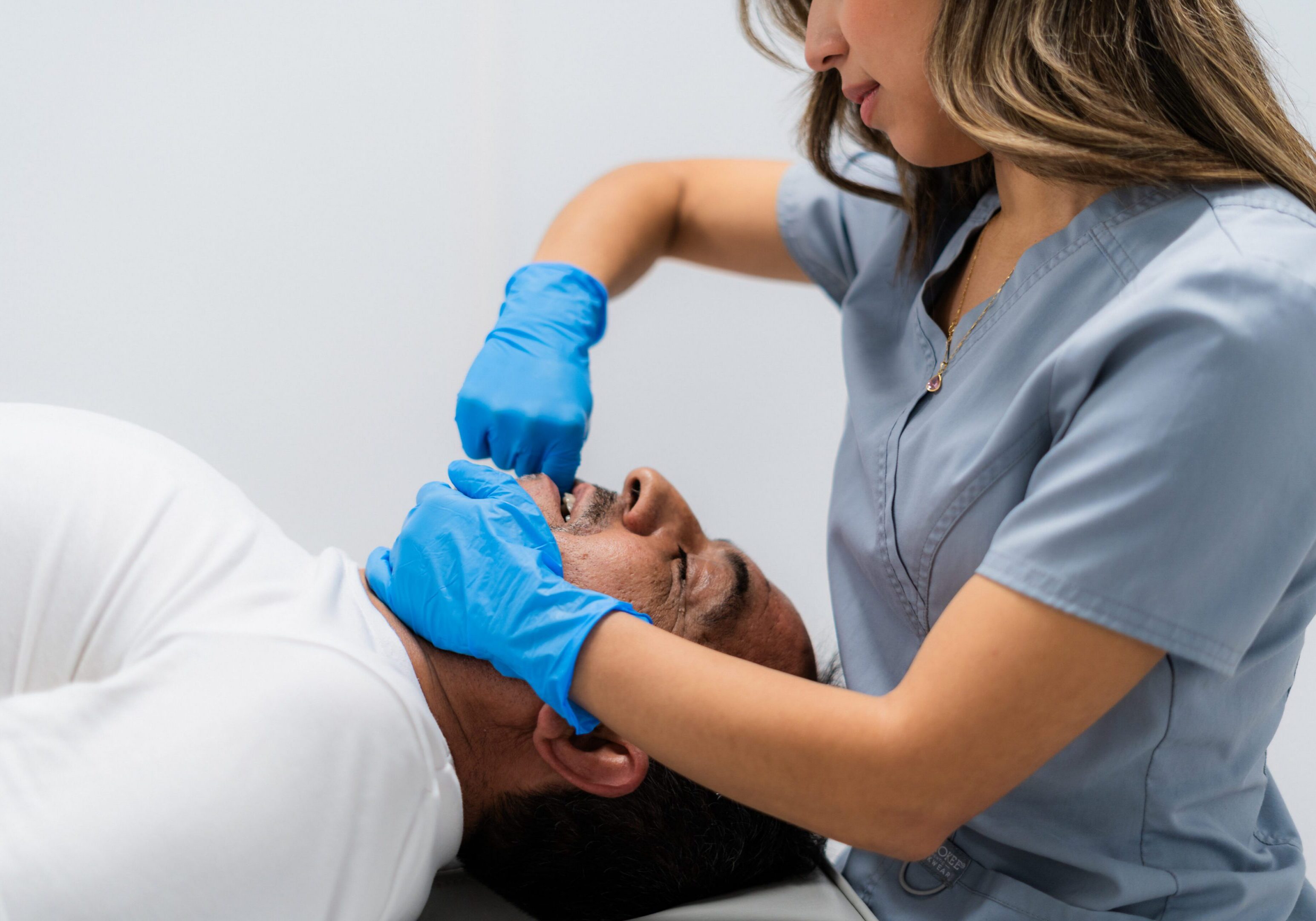 Young adult physiotherapist massaging jaw of a mature adult patient lying down