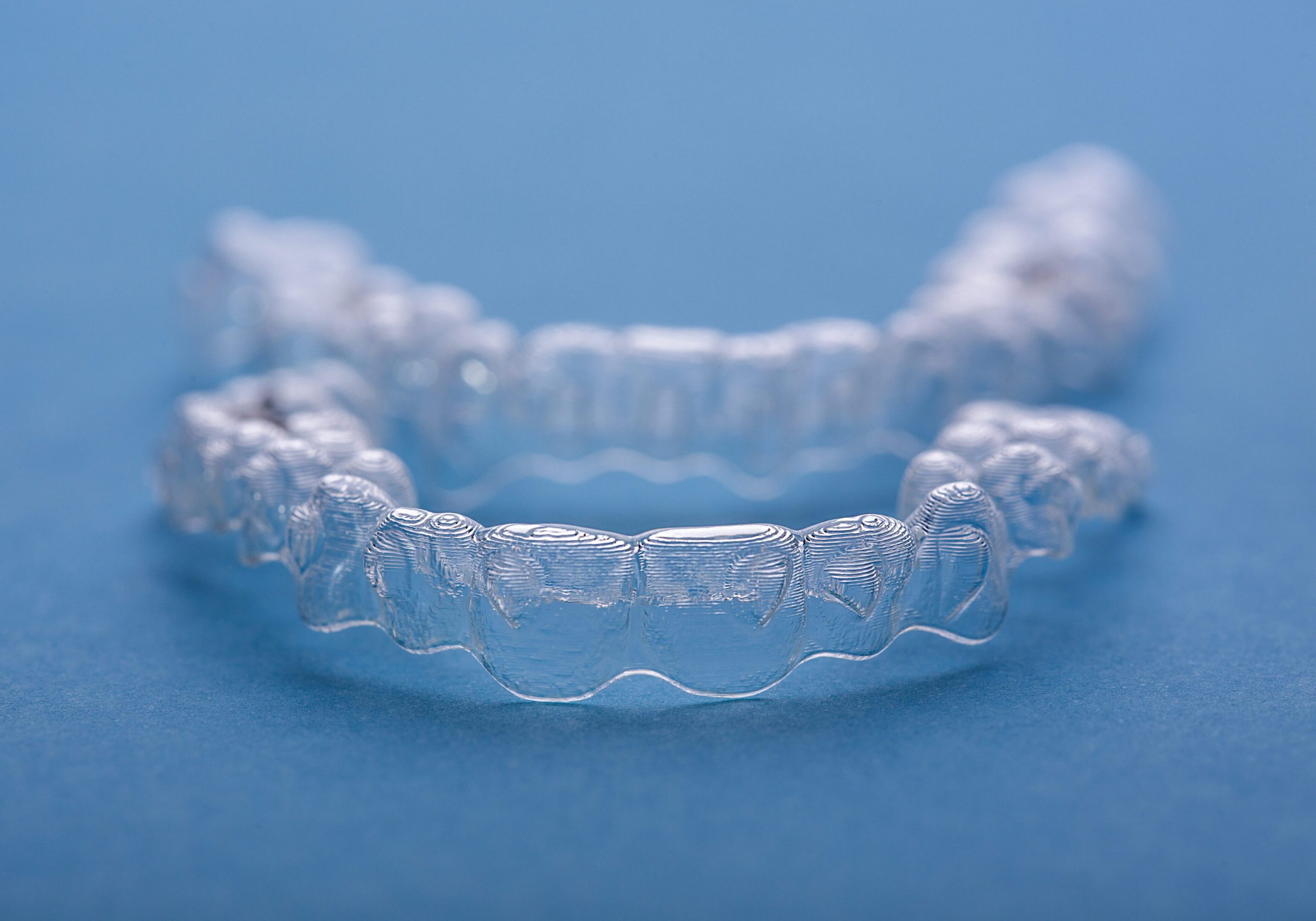 Close-up view of transparent orthodontic aligners arranged on a vibrant blue surface, showcasing their precise design